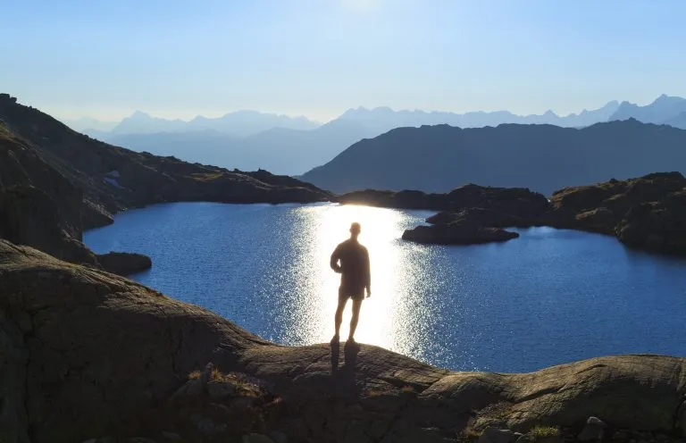 Homme regardant un lac, le lac Cornu, en direction du soleil.